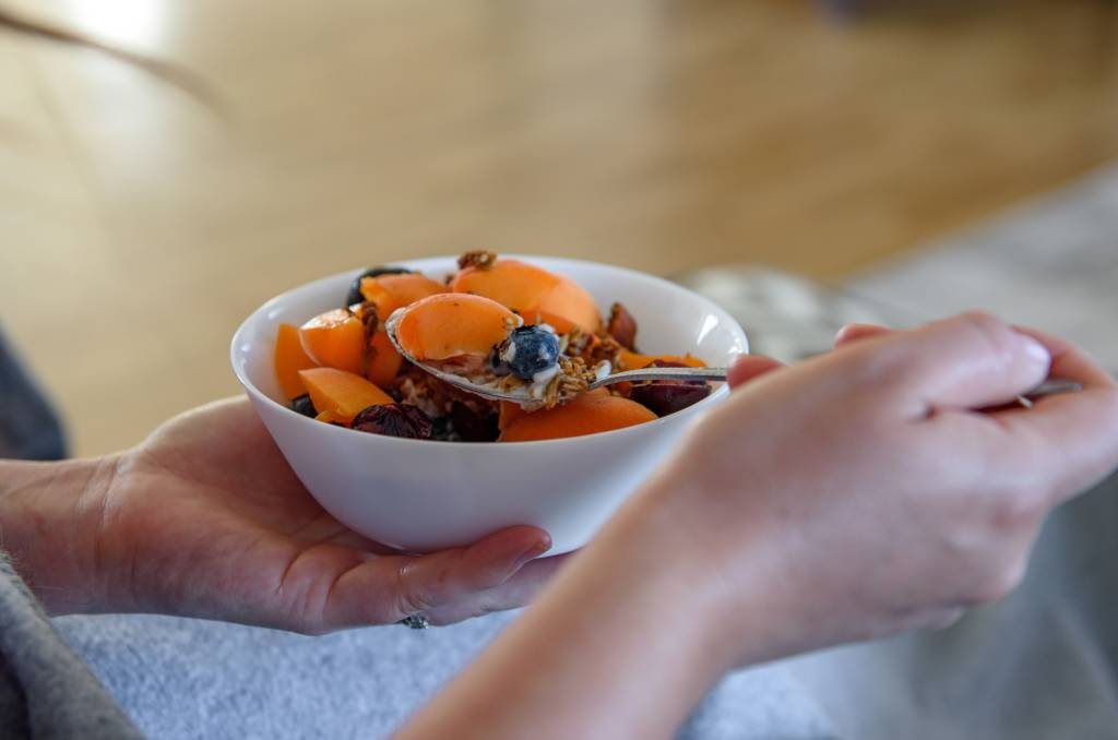 Close-Up Photo Of Woman Eating Overnight Oats Breakfast With Apricots, Blueberries And Granola aveia amanhecida