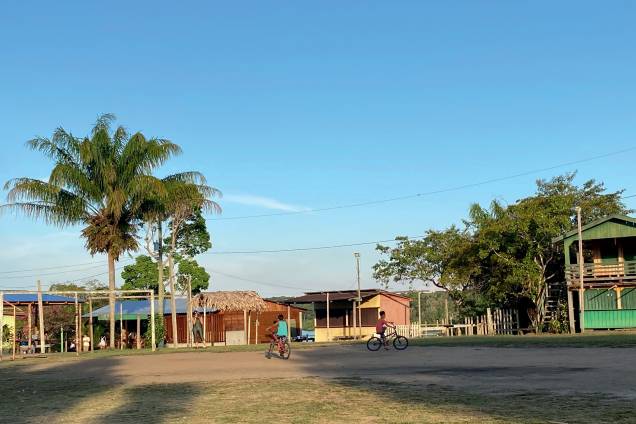 Duas crianças pedalam numa clareira da comunidade de Tumbira, formada por casas de madeira multicoloridas. Duas crianças pedalam numa clareira da comunidade de Tumbira, formada por casas de madeira multicoloridas.