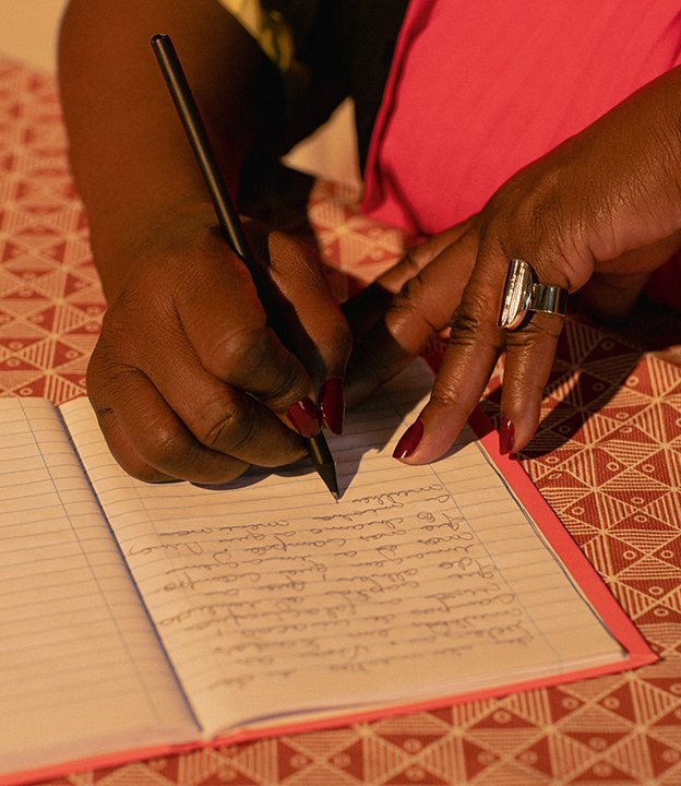 Conceição anota suas inspirações num caderno vermelho. Ela usa vestido do Apartamento 03 e anel, Zâmbia.