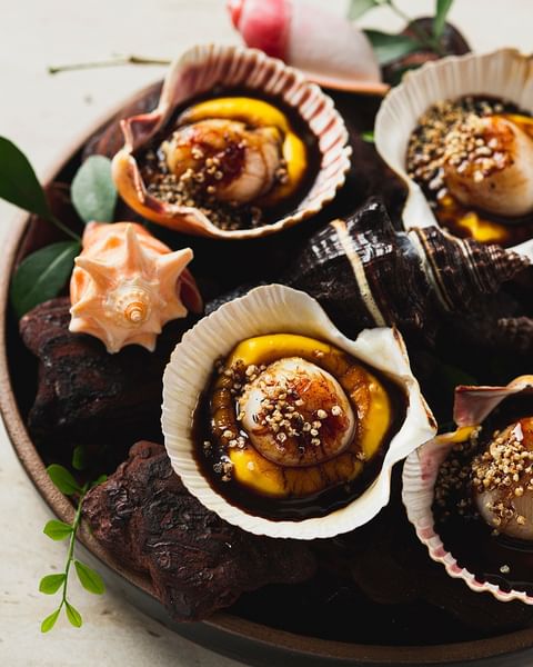 As Conchas Tucupi são recheadas com vieiras frescas, feitas na chapa em sal de alho, acompanhadas com purê de abóbora, mel de tucupi preto e rapadura
