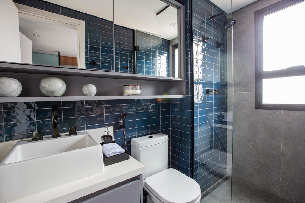 Banheiro retrô com revestimentos no tom de azul, com armários nichados e cuba retangular