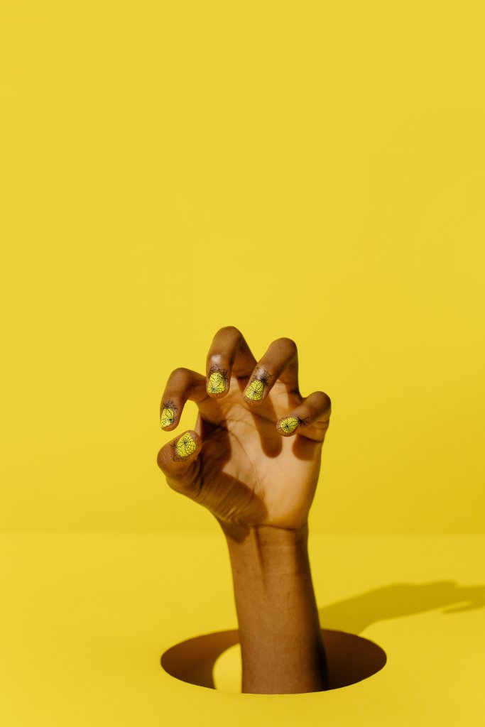 Mão com unhas decoradas no fundo amarelo