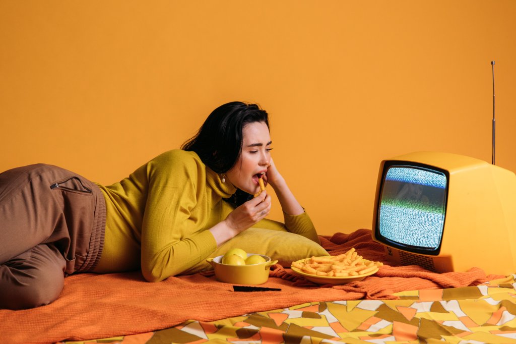 Mulher comendo cenourinhas em frente a uma TV