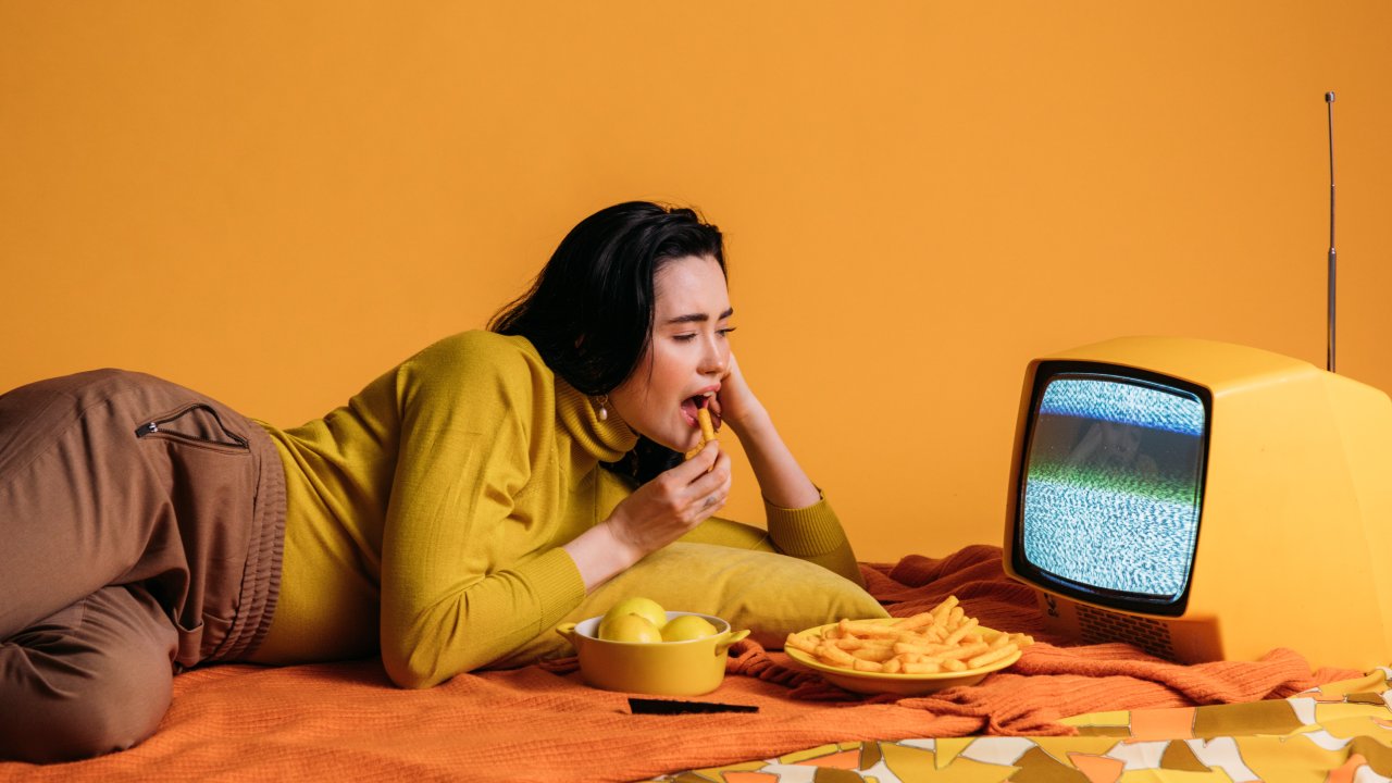 Mulher comendo cenourinhas em frente a uma TV