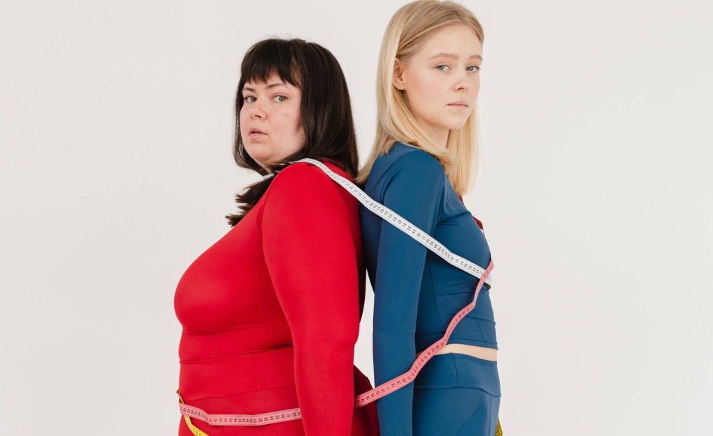 Duas mulheres, uma gorda e uma magra, juntas, com uma fita métrica ao redor do corpo