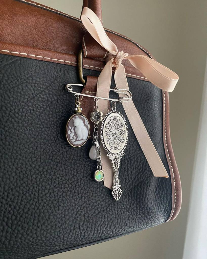 bag-charms-trend-acessórios-bolsas-laços-pingentes-tendência-TikTok Bolsa preta com detalhes em marrom e pingentes pessoais