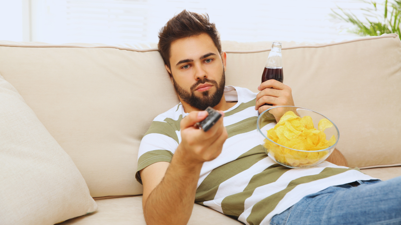 Homem no sofá com salgadinhos e refrigerante