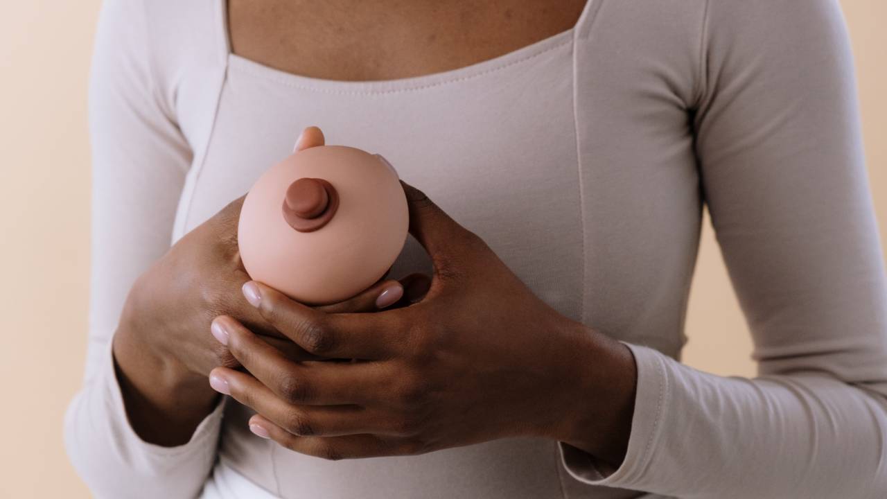 Mulher segurando um seio em miniatura a frente do corpo