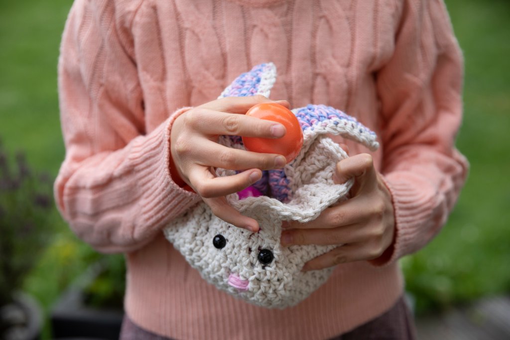 Menina segurando cestinha de tricô em formato de coelho
