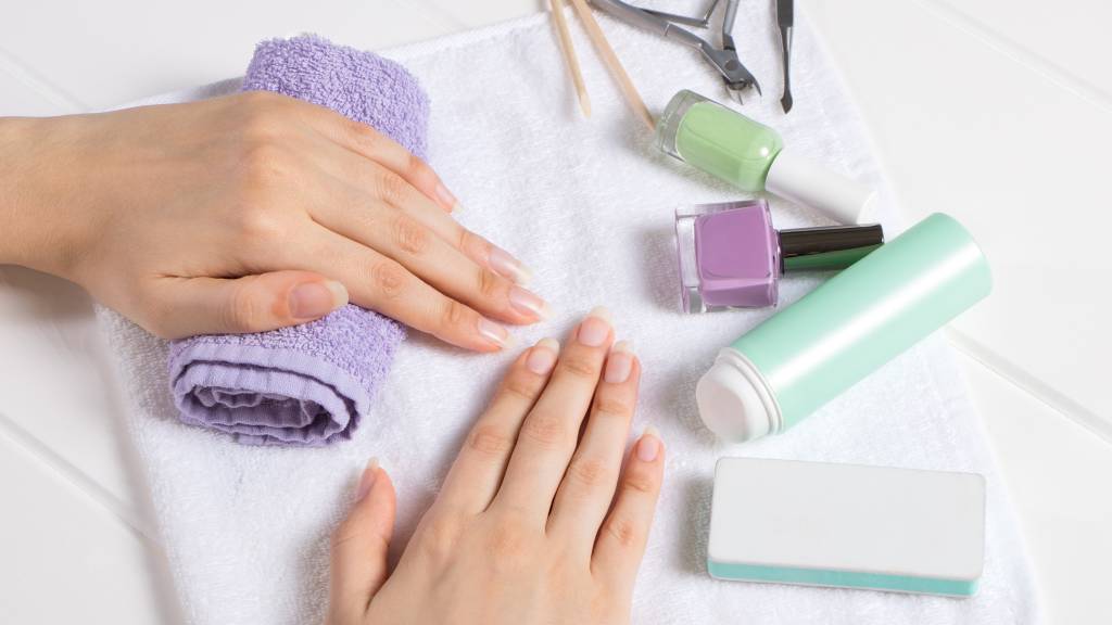 Comofazer-unhas-de-salao-em-casa-cutilagem-lixagem-e-corte.jpg Mulher com itens de manicure sobre uma mesa