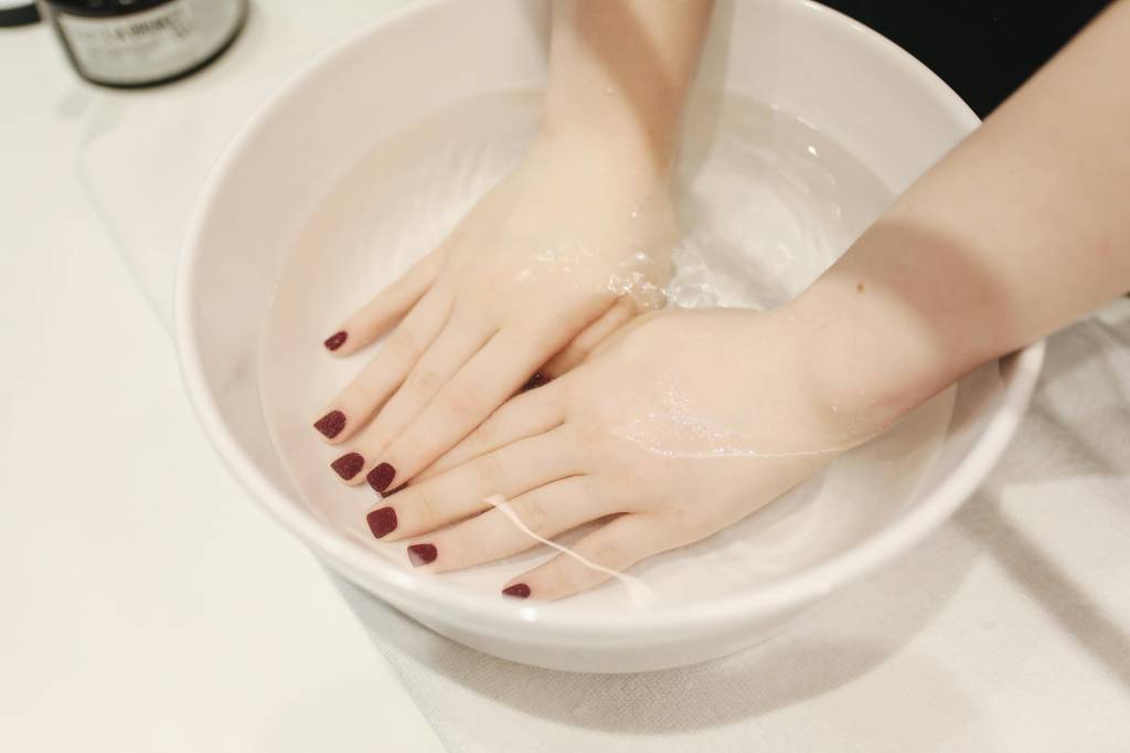 limpeza-das-unhas-passo-a-passo-sobre-como-fazer-unhas-de-salão-em-casa Mulher colocando as mãos em um recipiente com água