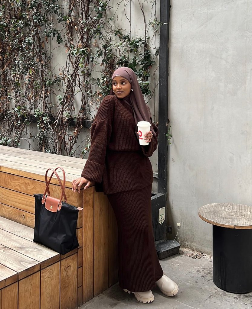 A foto mostra um mulher vestindo um conjunto de tricô marrom, pareado com um hijab da mesma cor