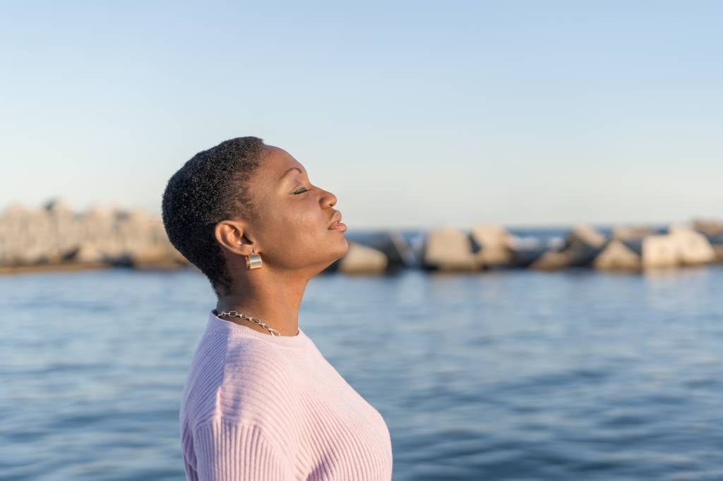 Mulher negra sorrindo com melancolia junto ao mar, sugerindo emoções de resiliência