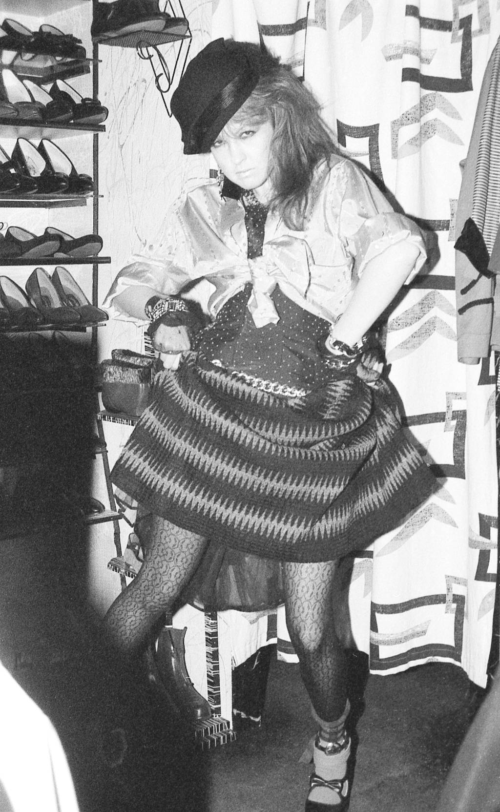 Let The Canary Sing cindy lauper em foto preta e branca. Ela tem os cabelos escuros e médios, presos em um rabo de cavalo lateral. Ela veste uma saia listrada e meia-calça