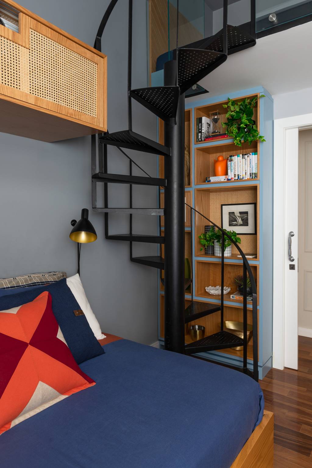 decoracao-escada-caracol foto mostra uma sala cinza, com escada caracol de metal preta. Ao lado, uma pequena estante de marcenaria completa o espaço