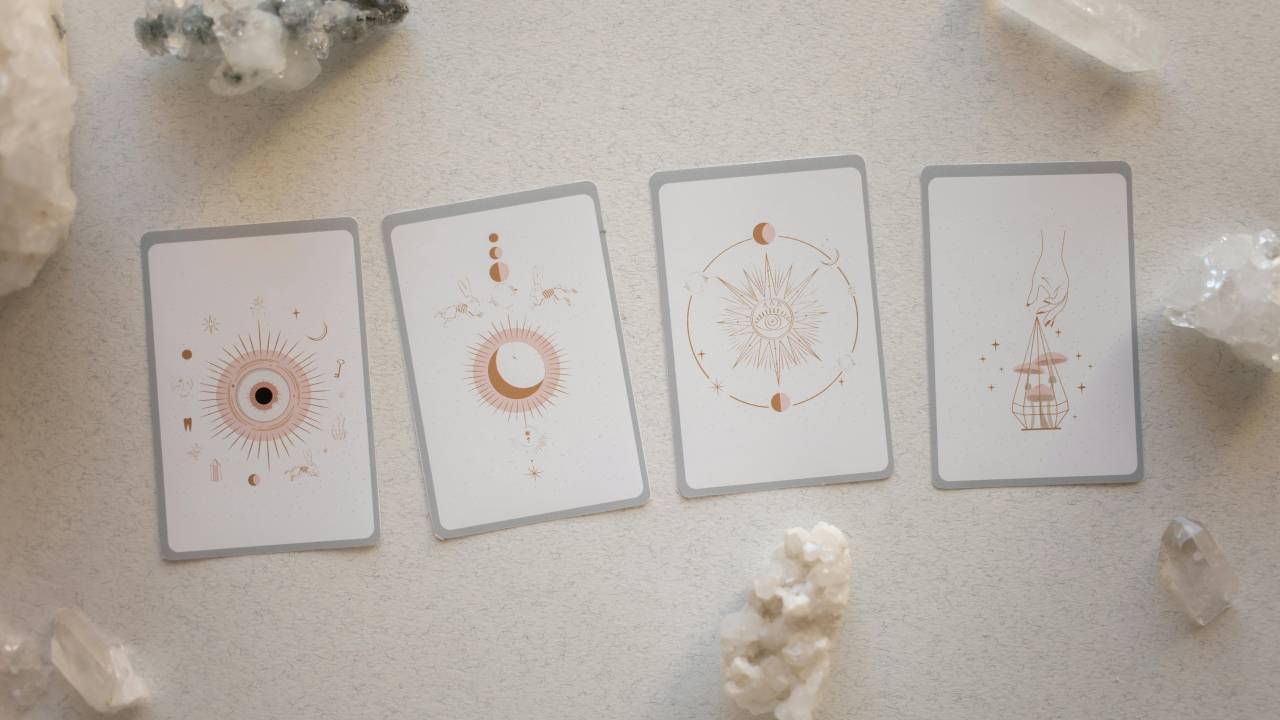 Mesa branca com cristais e cartas representando signos do zodíaco, descritos no horóscopo da semana