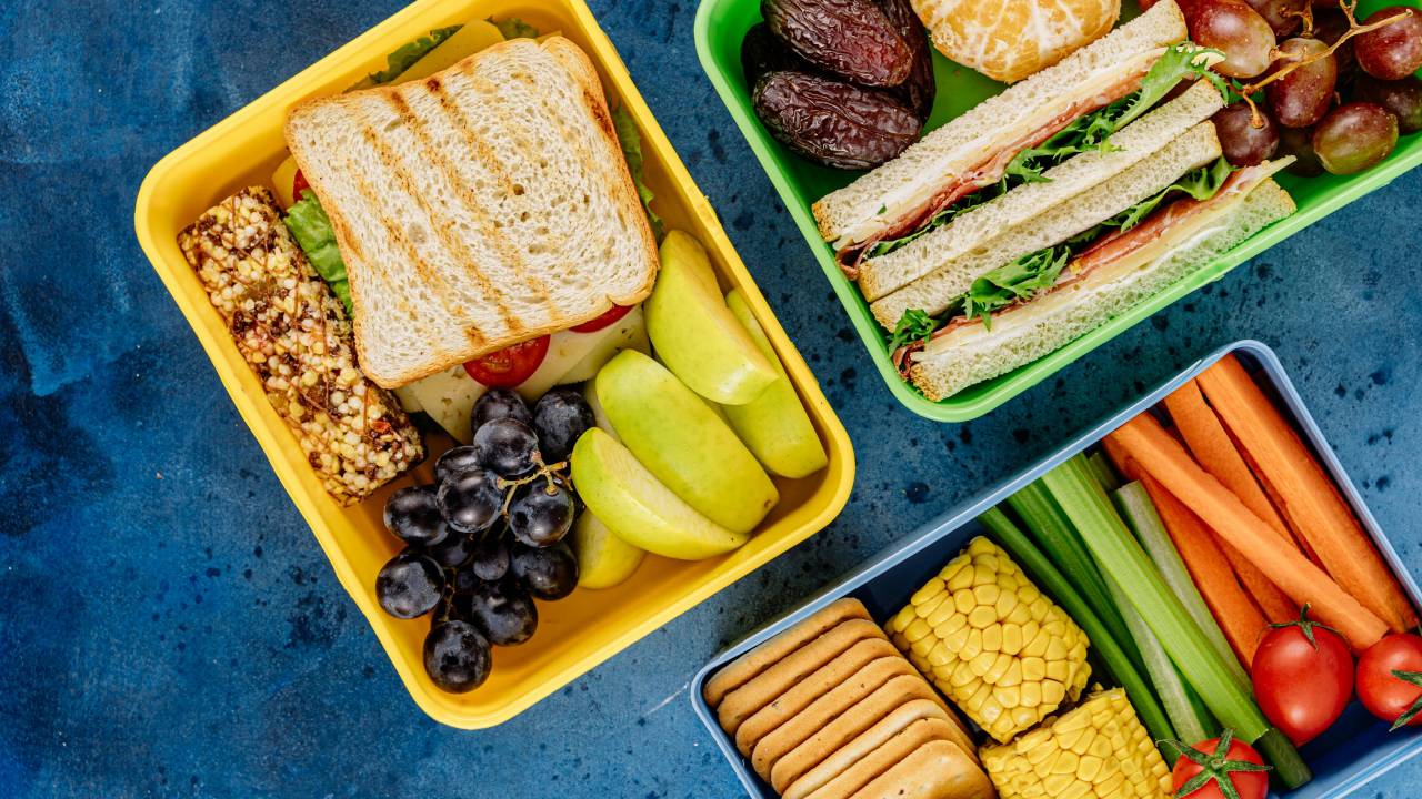 Foto de potes de plástico com comida saudável dentro, como sanduíches, frutas e bolachas