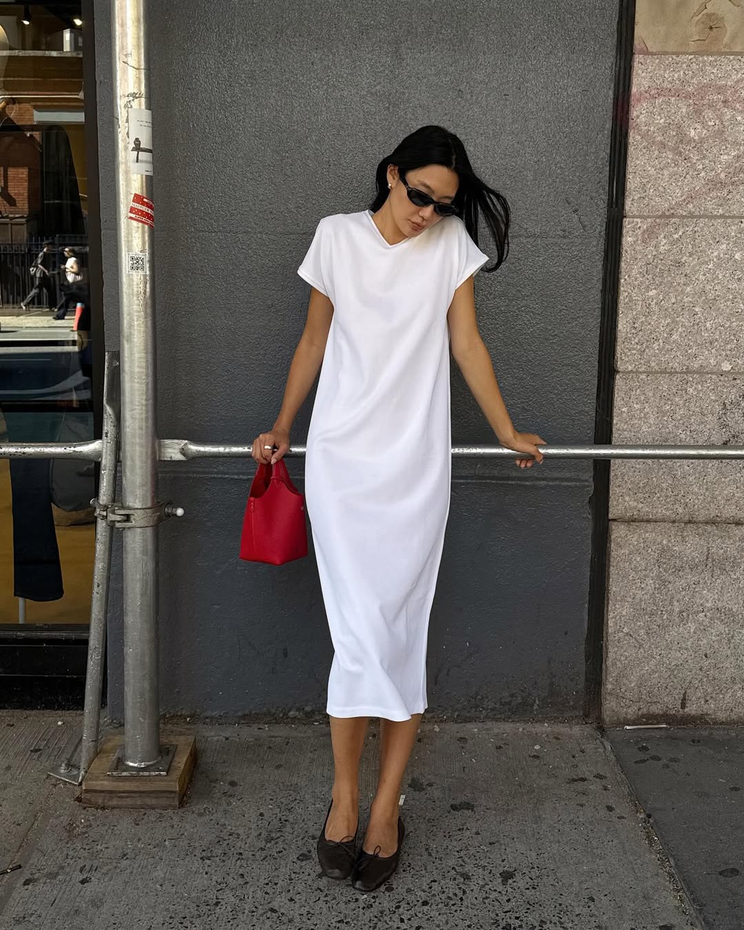Foto de uma mulher amarela usando um look composto por vestido branco, bolsa vermelha, &oacute;culos de sol e salto preto