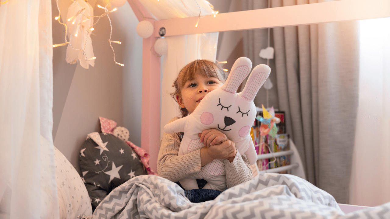 Menina em cima da cama abraçada com um urso de pelúcia em quarto infantil.