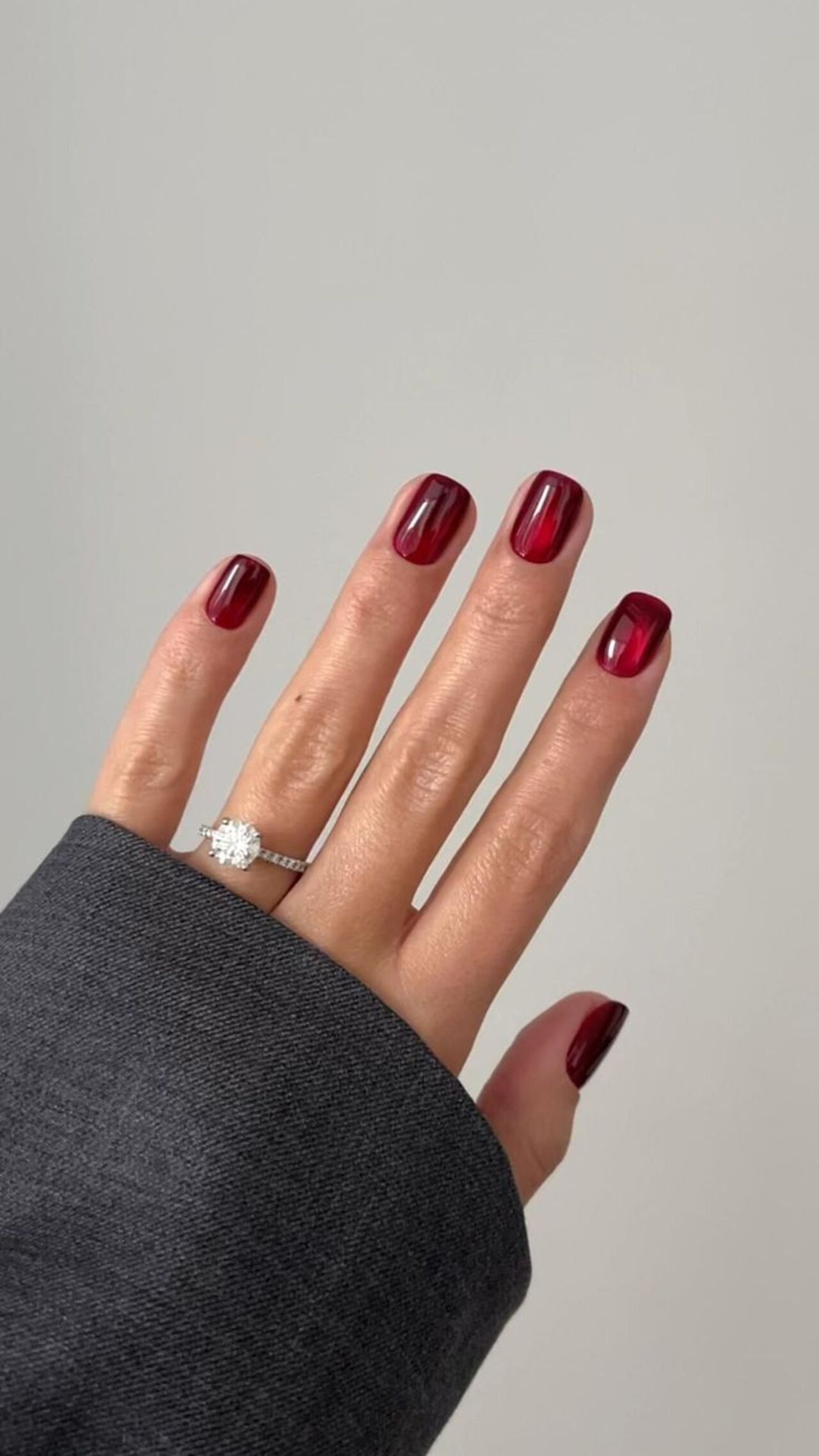 Unhas curtas com esmaltação bordô holográfica.