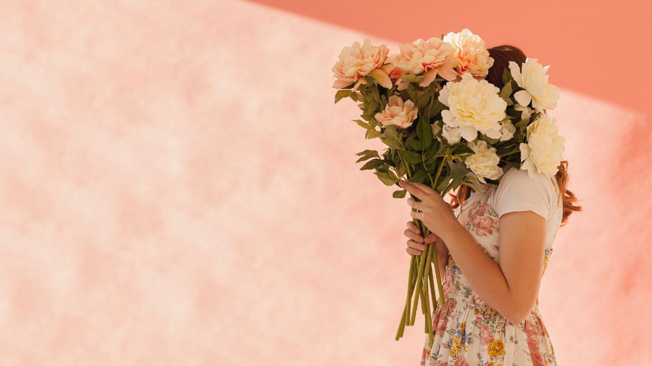 Imagem de mulher vista de lado segurando flores em frente ao rosto