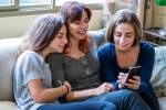 Duas filhas mostrando algo no celular para a mãe.