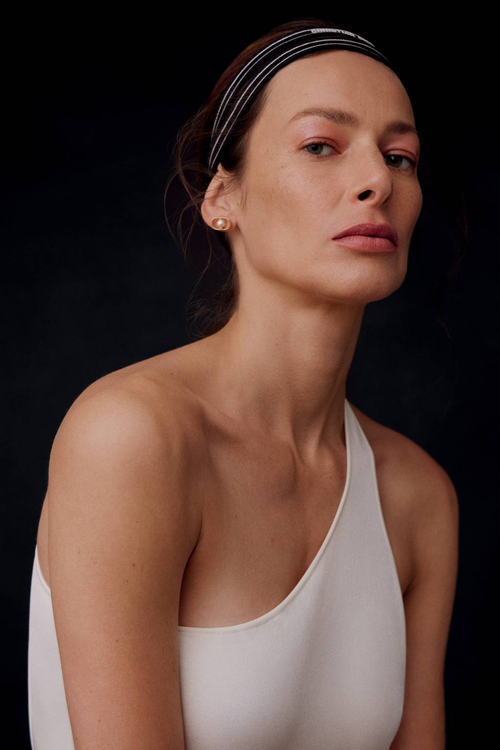 imagem vertical_beleza dior2 Imagem de mulher branca exibindo maquiagem delicada e feminina. O fundo é preto e ela usa uma regata de manga única.