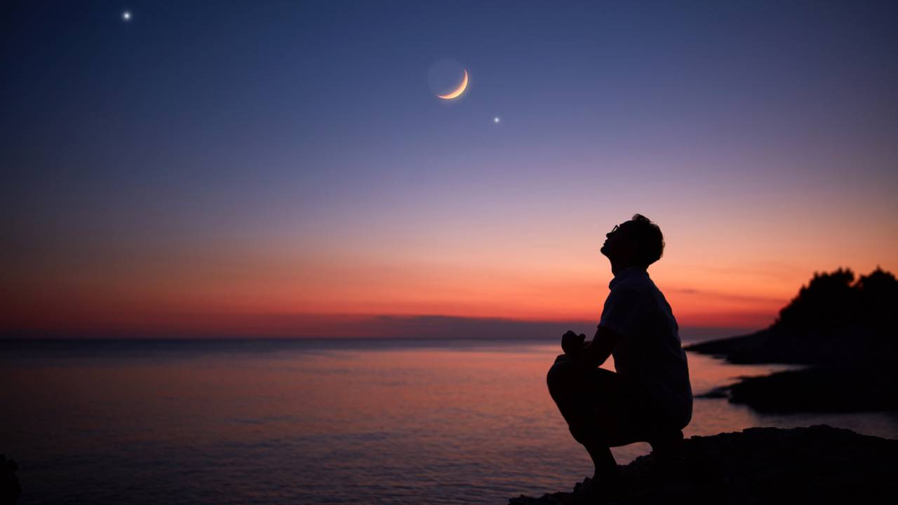 Silhueta de um homem olhando para a Lua e estrelas sobre o horizonte do oceano marinho.