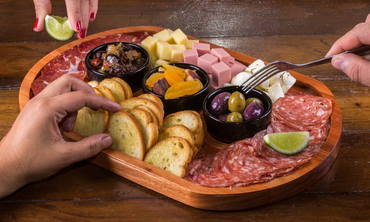 Pães, frios, queijos, azeitonas e antepastos compõem uma tábua de frios acessível