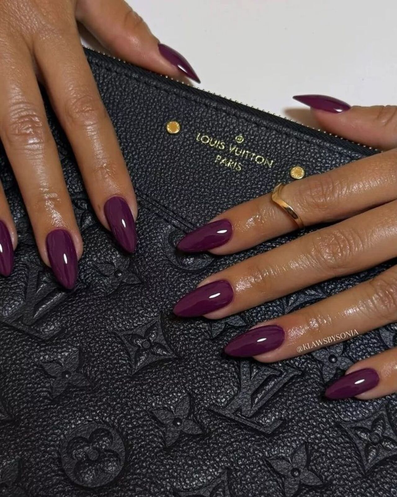 Imagem de mão branca com unhas amendoadas com esmaltação roxo berinjela.