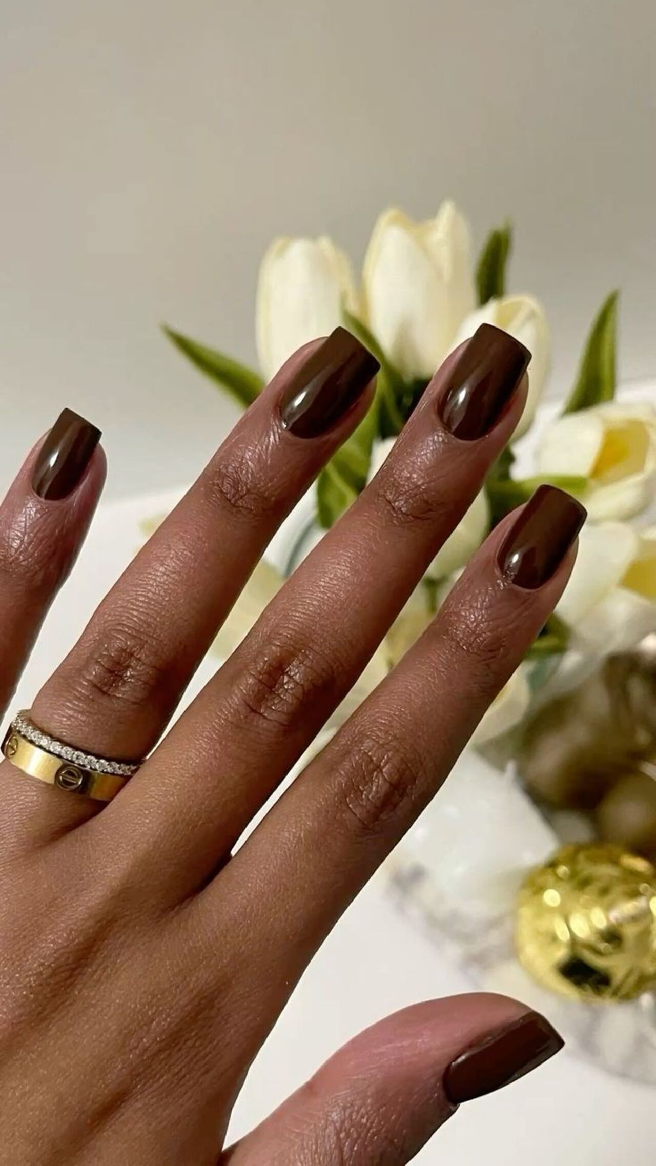 Imagem de mão negra com unhas quadradas com esmaltação marrom.