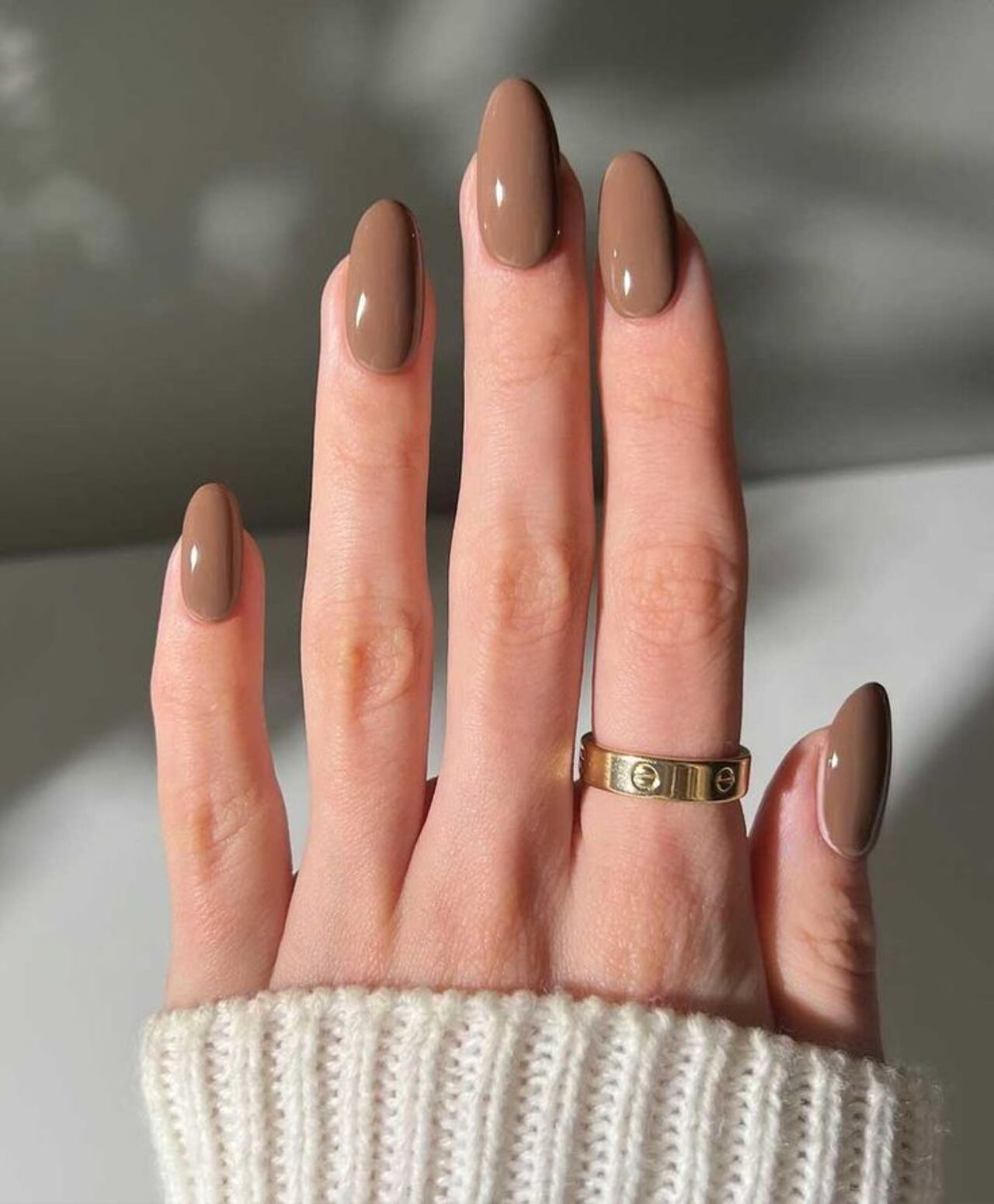 Imagem de mão branca com unhas amendoadas com esmaltação mocha mousse.