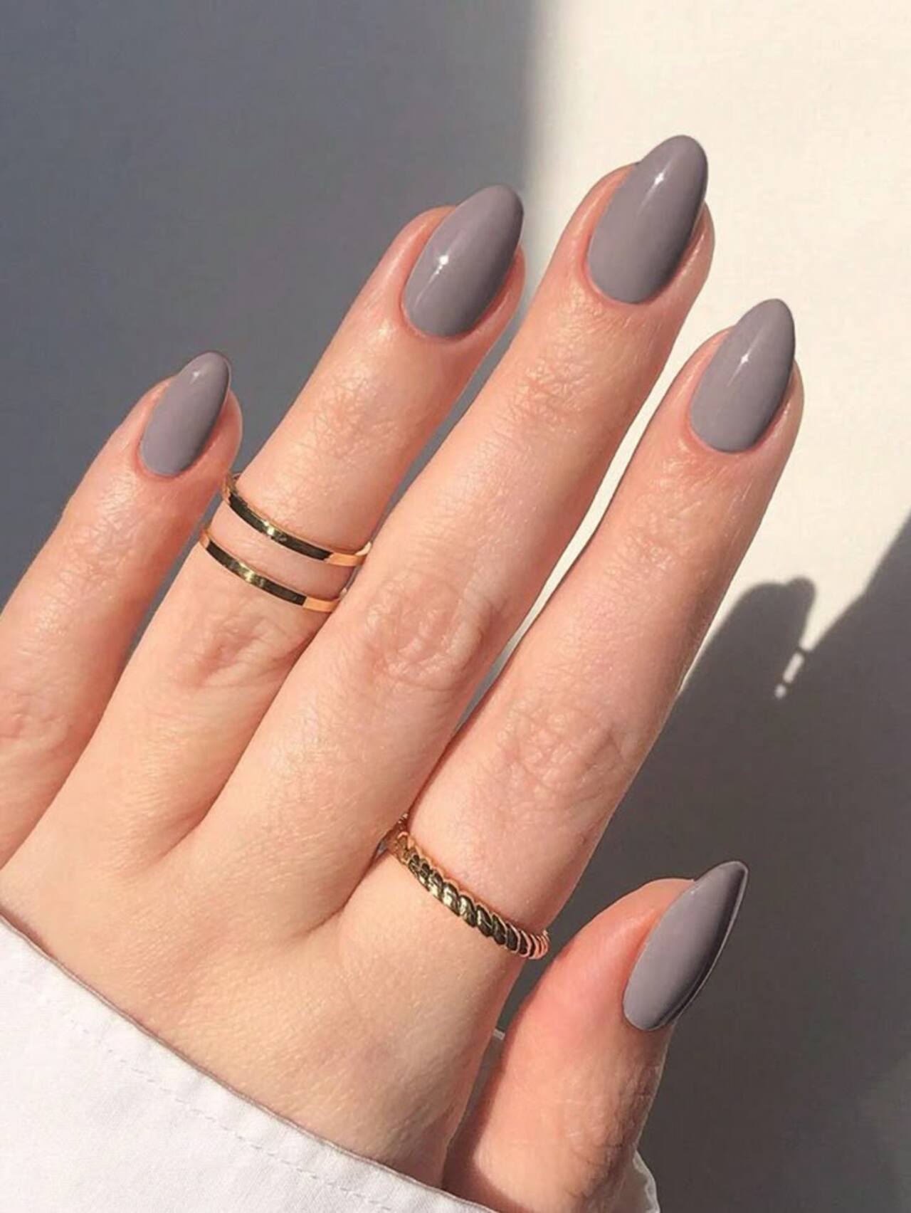 Imagem de mão branca com unhas amendoadas com esmaltação cinza claro.