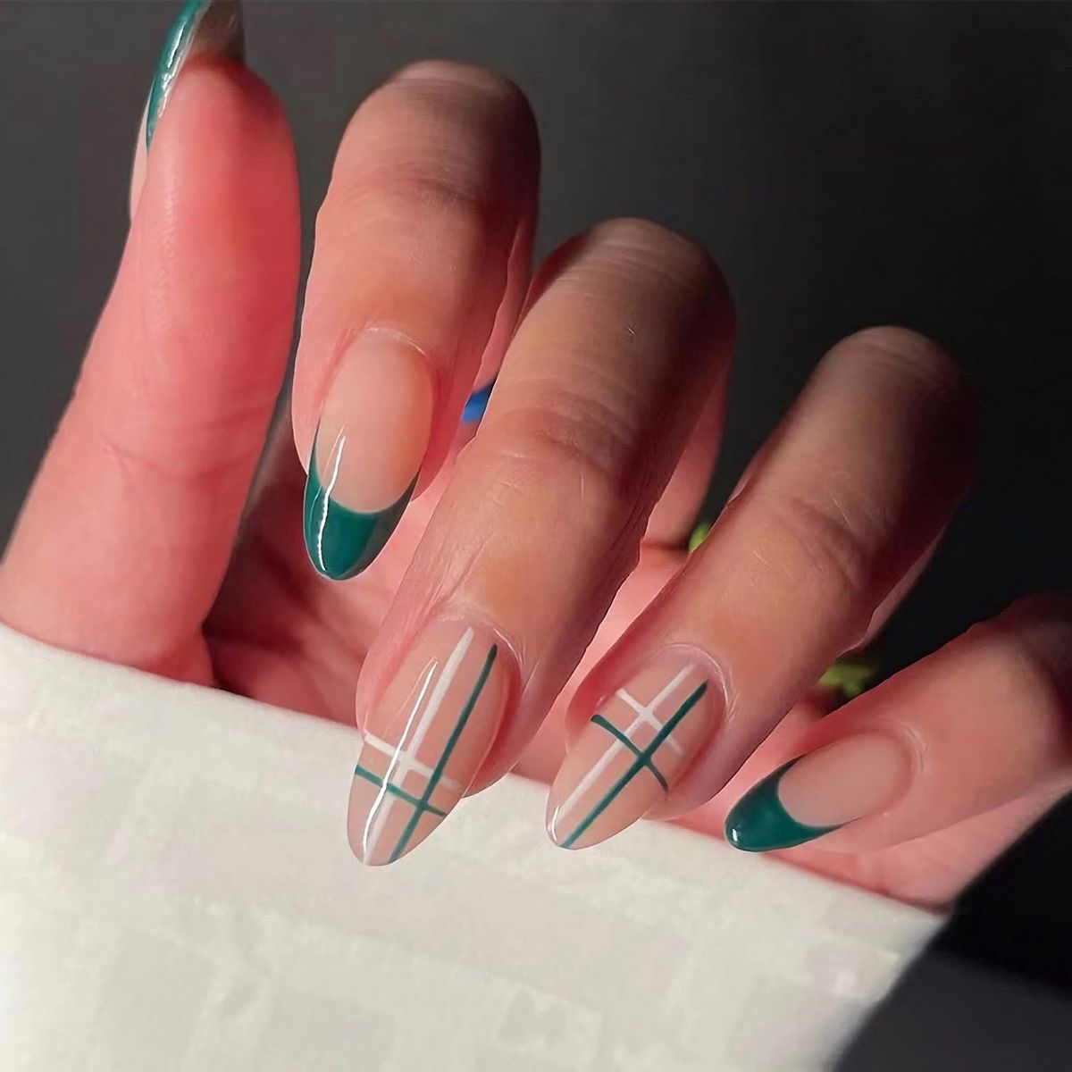 Imagem de mão exibindo unhas com francesinha e decoração xadrez verde.