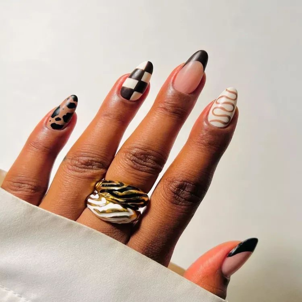 Imagem de mão exibindo unhas com diversas estampas como xadrez, animal print e linhas.