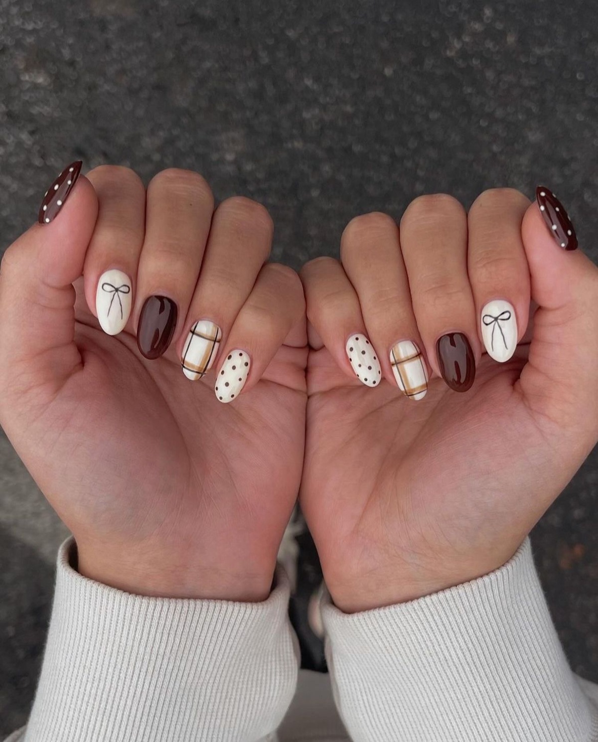 Imagem de mão exibindo unhas com diversas decorações como lacinho, xadrez e bolinhas.