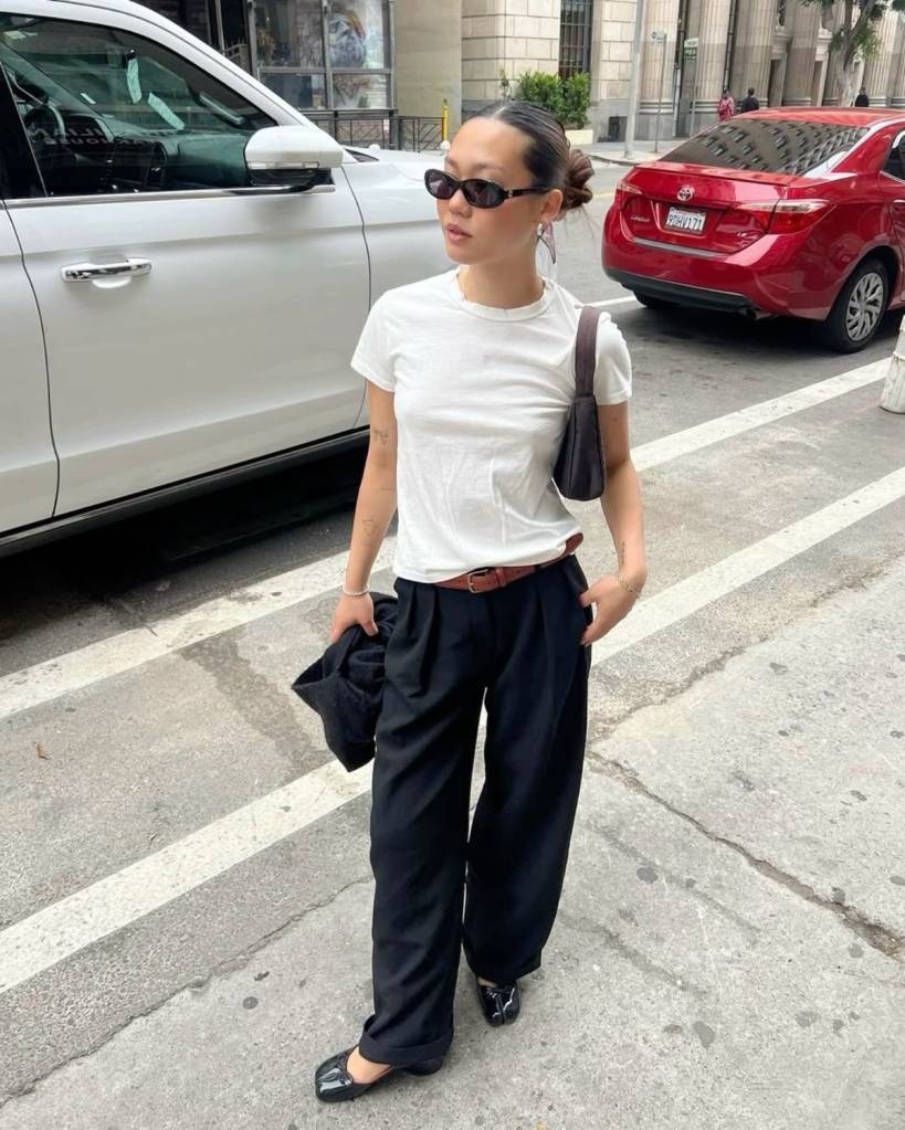 Pessoa usando camiseta branca e calça de alfaiataria larga preta, combinadas com sapato tabi branco e cinto escuro. Look clean com toque contemporâneo.