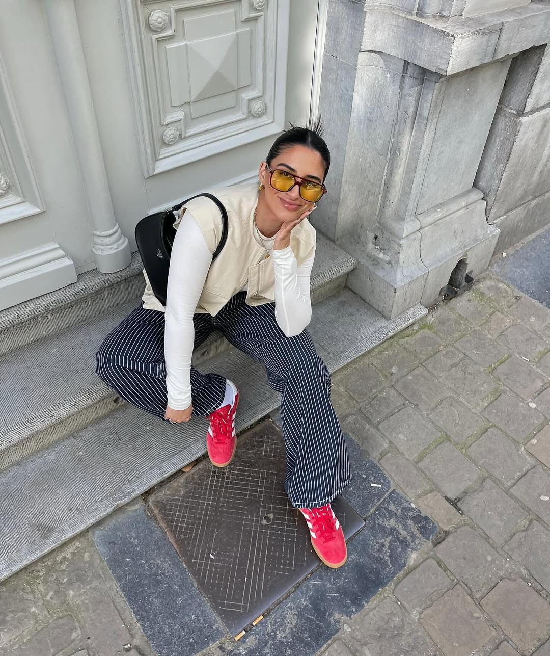 Look com calça listrada, colete bege e tênis vermelho