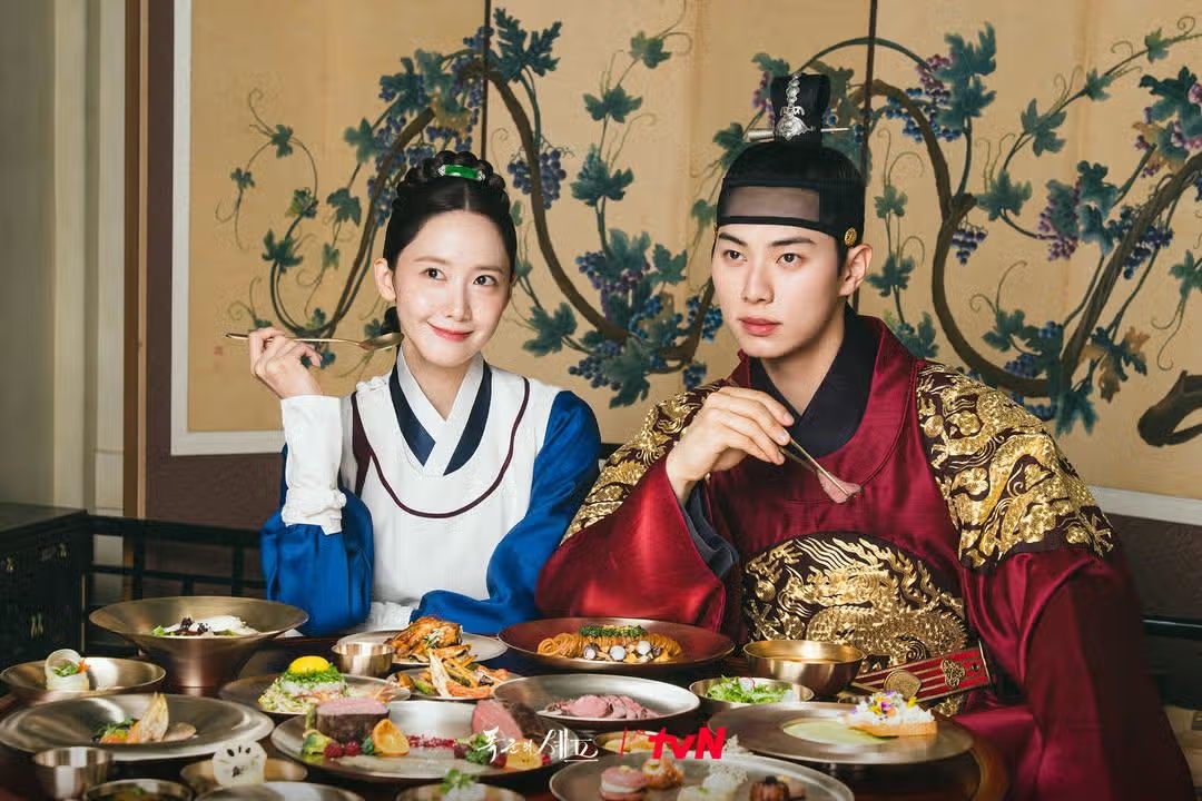 Imagem de casal coreano com mesa farta em cena de Bon Appétit, Vossa Majestade
