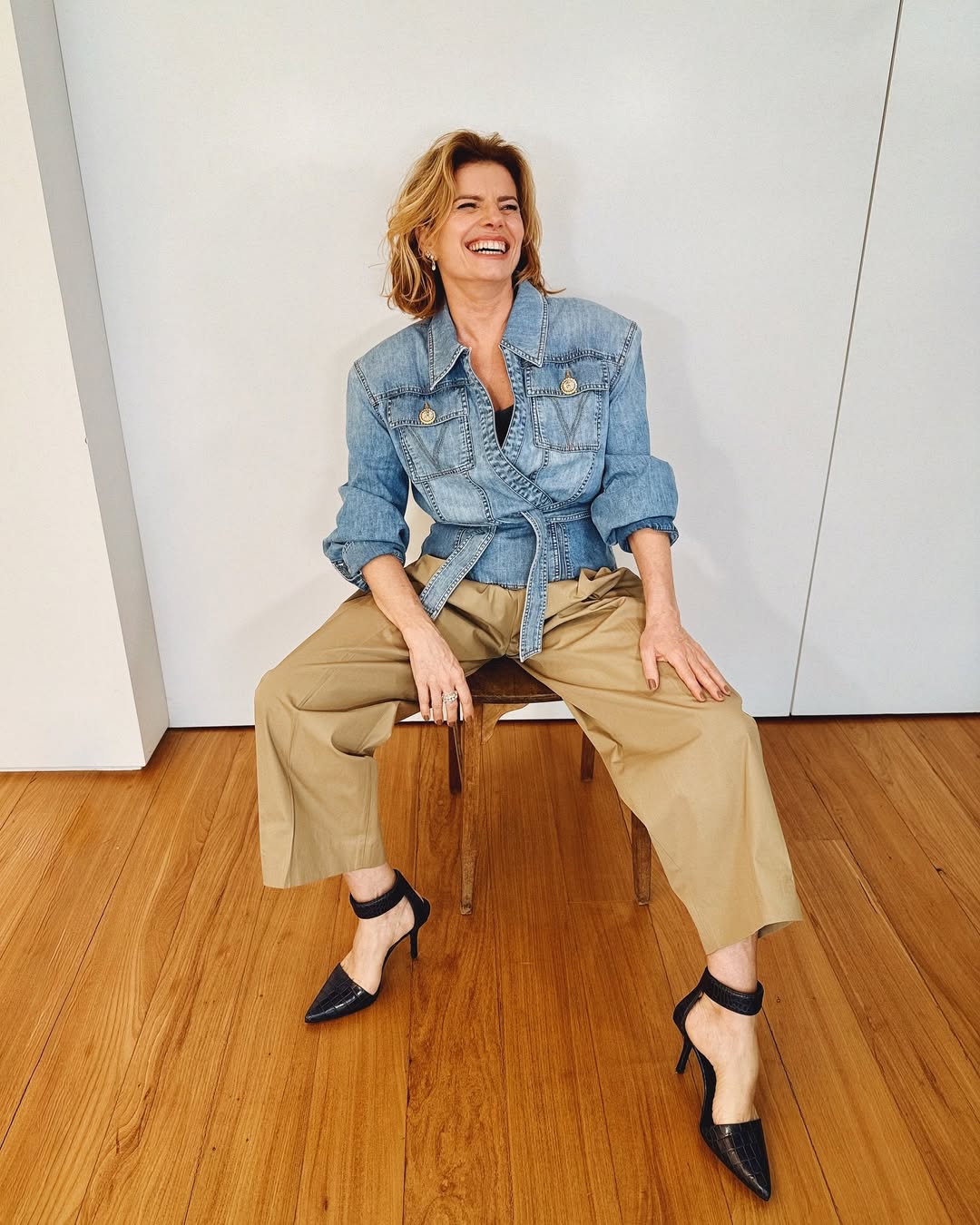 Foto de Debora Bloch usando um look composto por jaqueta jeans, calça de alfaiataria marrom e salto scarpin preto