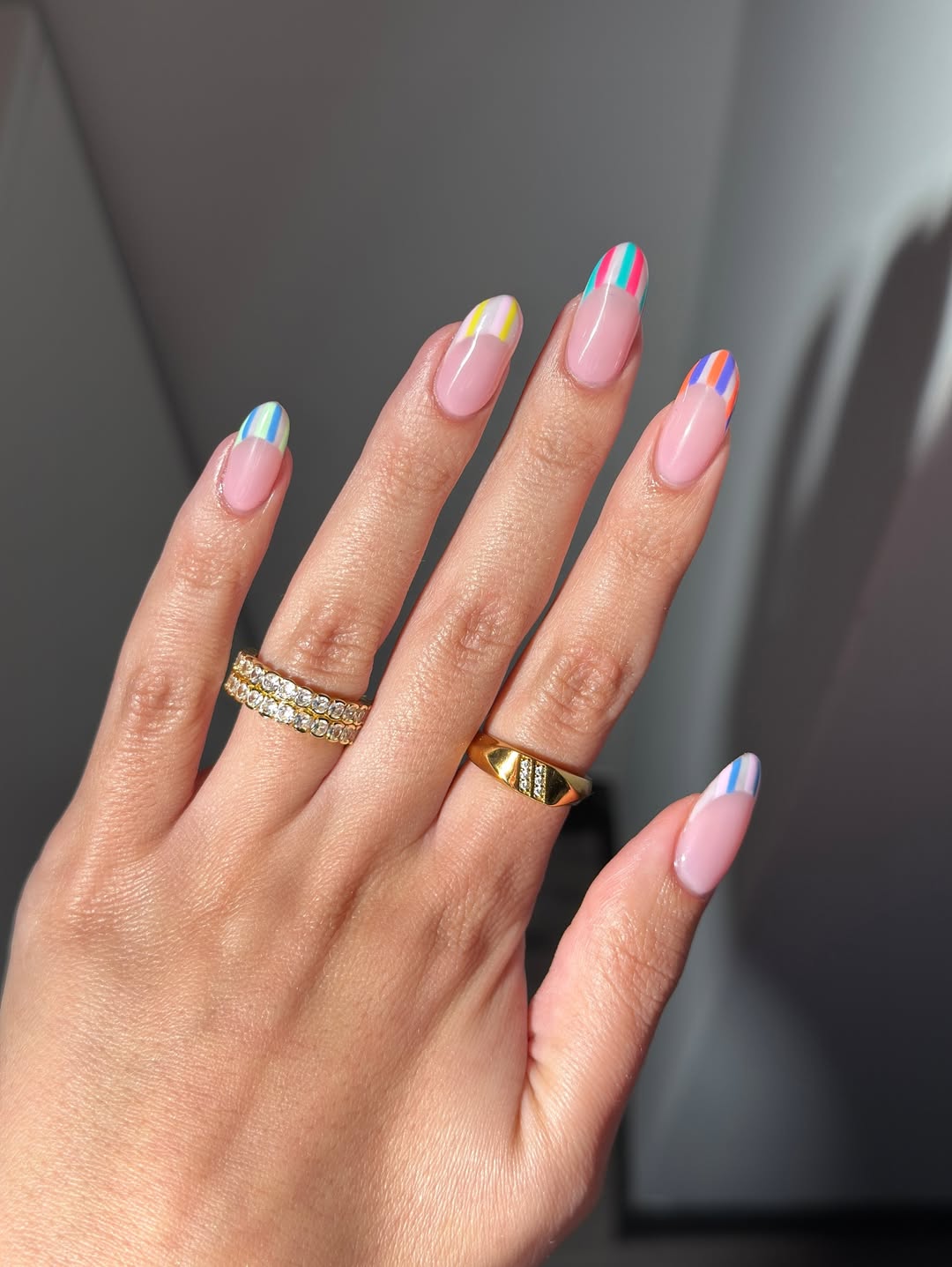 Foto de uma mão com as unhas amendoadas. As unhas estão com a nail art de uma francesinha em listras coloridas