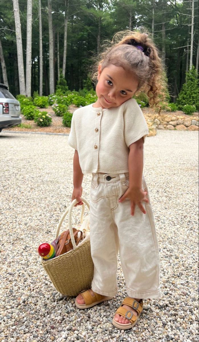 Foto de uma menina negra usando um look composto por casaqueto, calça jeans branca e cestinha de palha