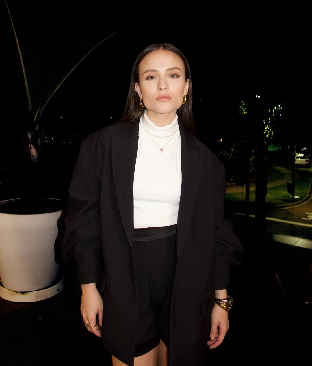 Foto de Larissa Manoela. Ela usa uma blusa de gola alta branca, um blazer preto e uma calça de alfaiataria preta