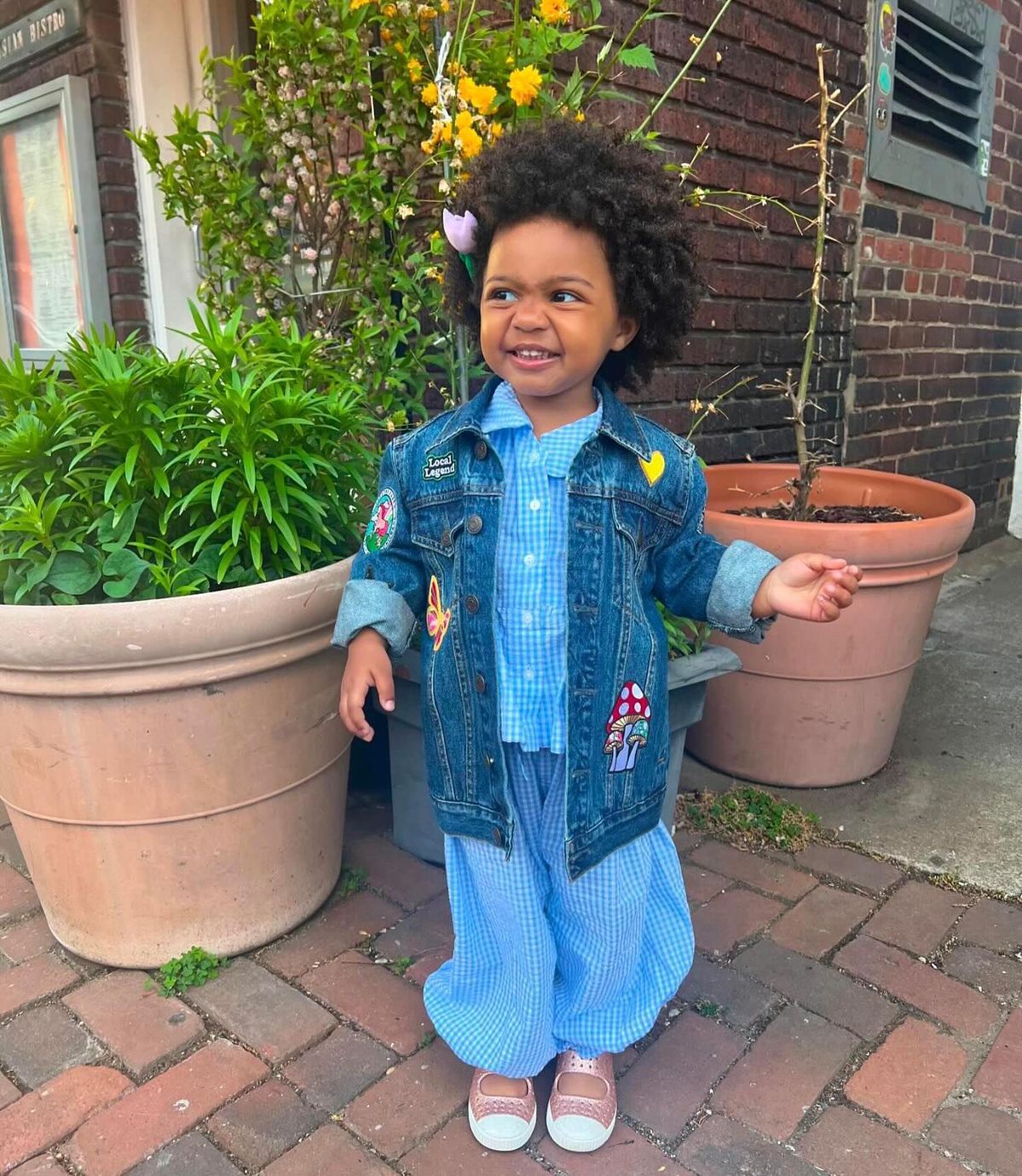 Foto de uma criança negra usando um look composto por jaqueta jeans, calça jeans e tênis