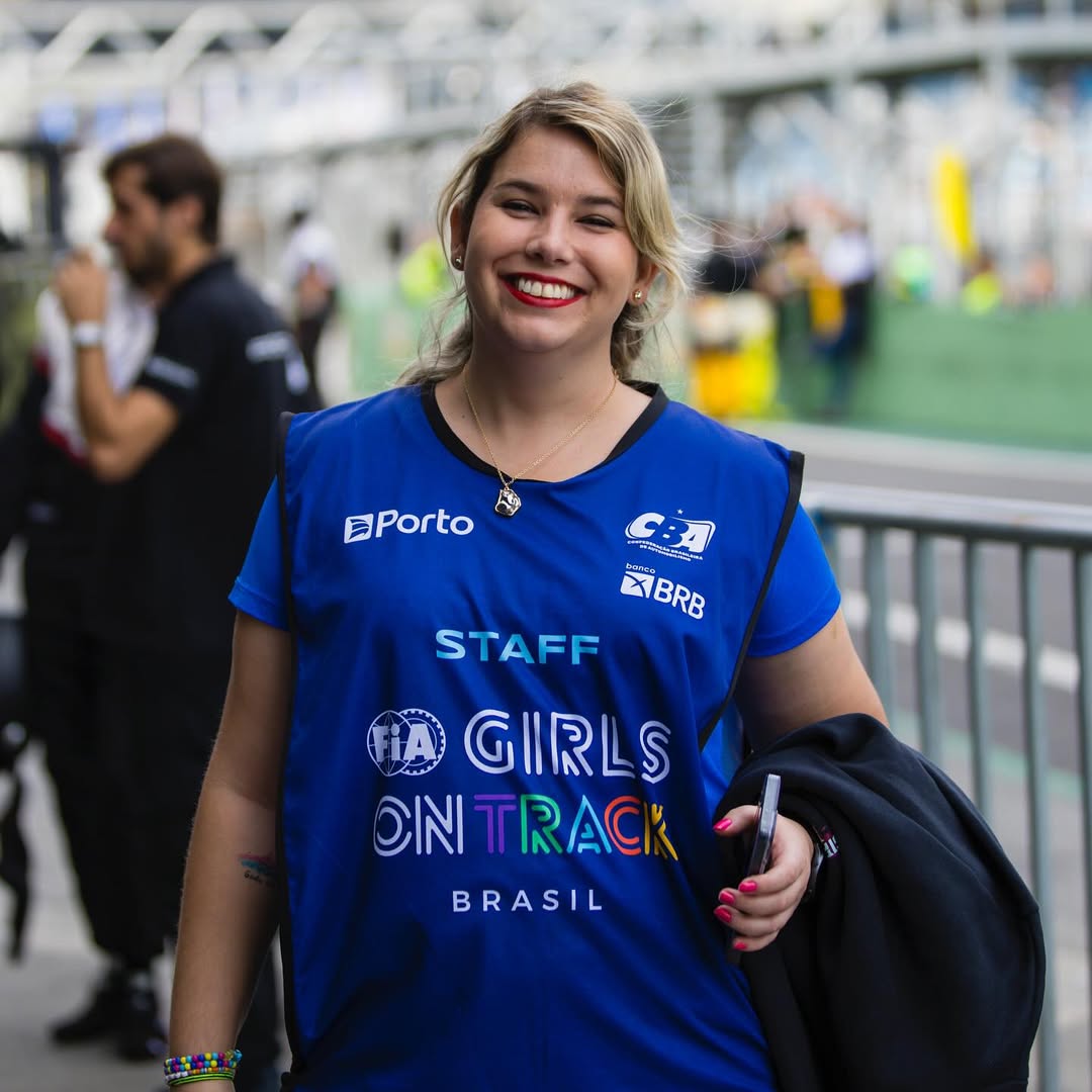 Mulher loira de cabelo preso e roupa azul em pista de corrida de carro.