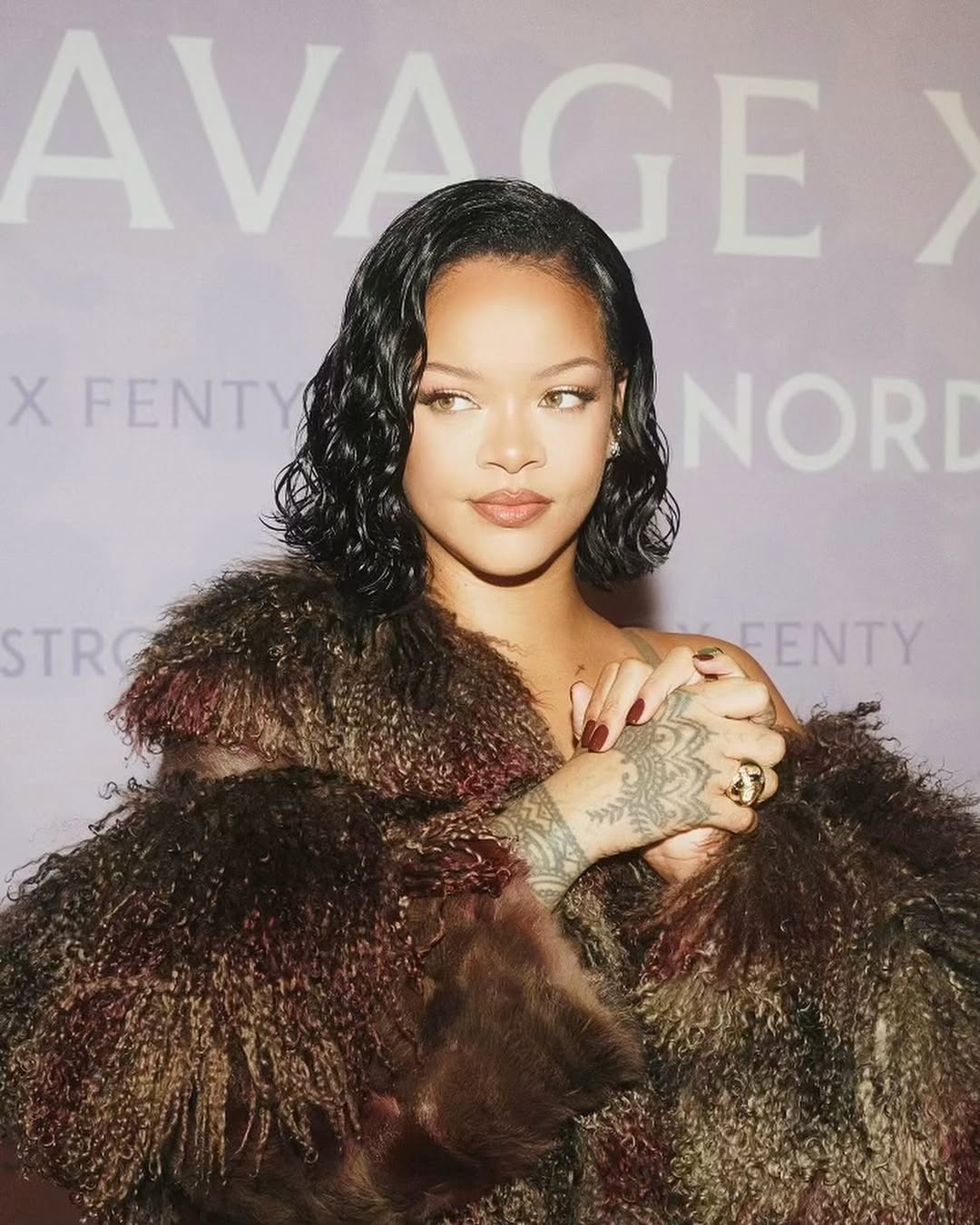 Foto de Rihanna. Ela est&aacute; com o cabelo preto, cacheado e brilhante e usa um casaco de pelos