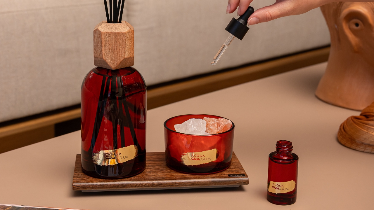 Aromatizante de ambiente, vela e conta gotas com embalagens vermelhas sobre mesa