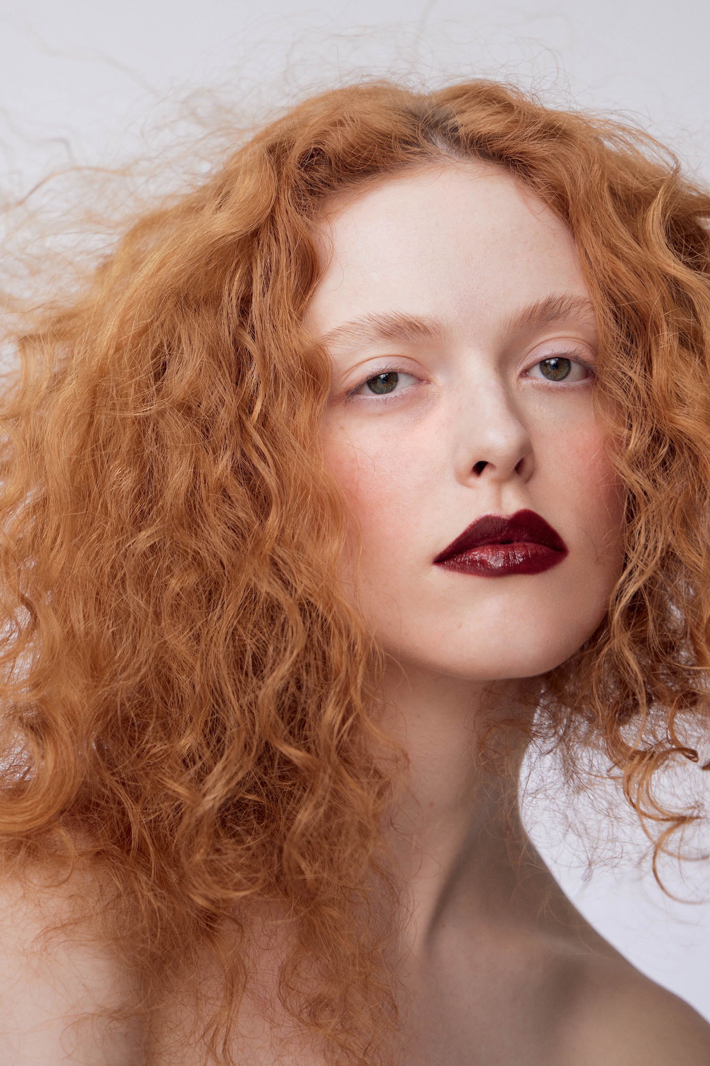 Modelo de pele branca e cabelos enrolados ruivos fazendo car&atilde;o para foto com batom vinho