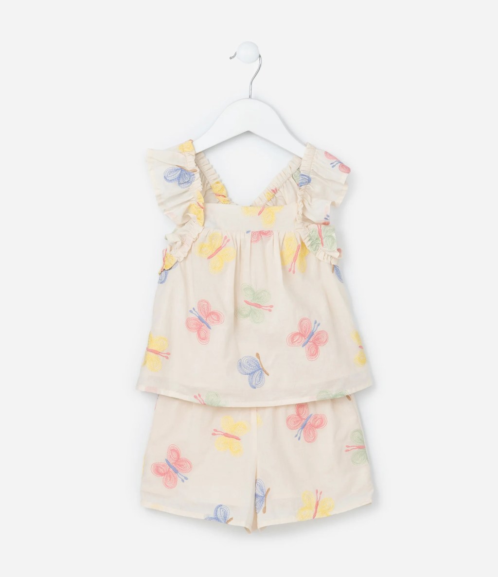Foto de um conjuntinho feminino composto por regata e shorts. O fundo &eacute; bege, mas h&aacute; uma estampa de borboleta por cima