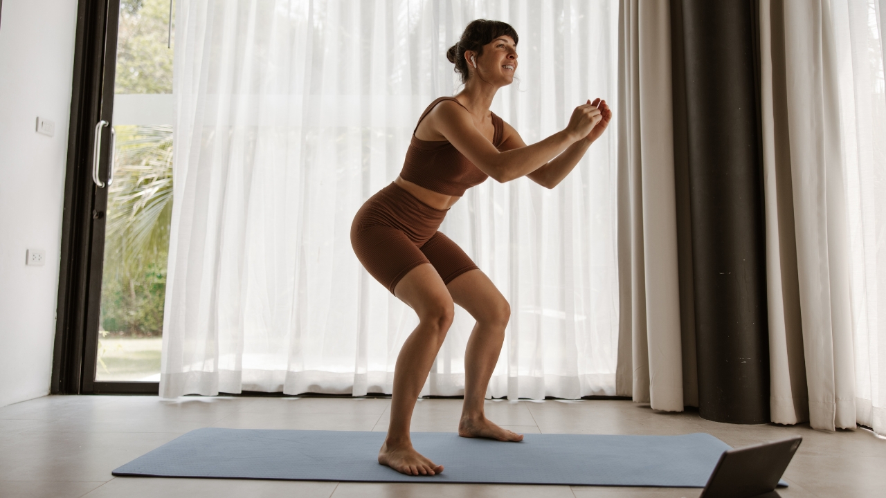 Mulher usando conjunto de treino marrom enquanto faz agachamento em casa